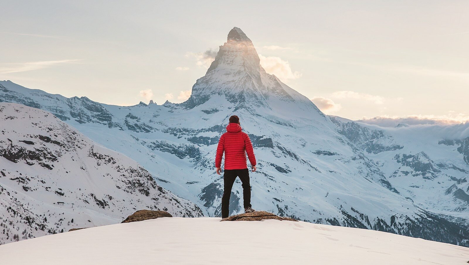 person in red hoodie standing on snowy mountain during daytime