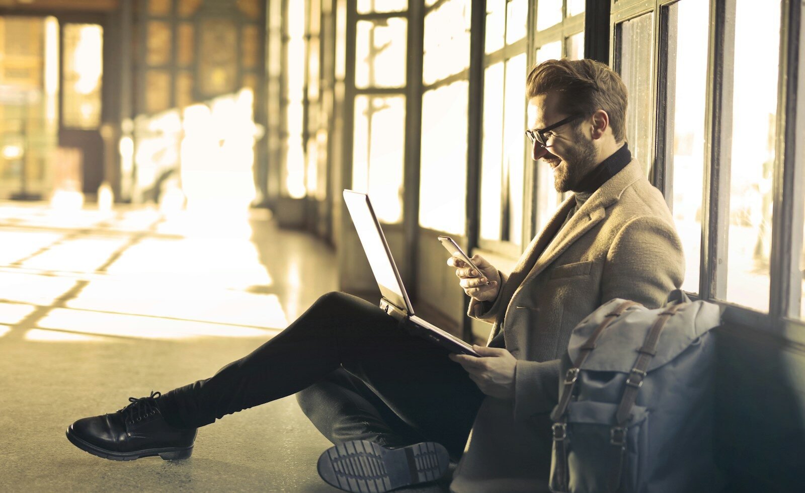 Airalo man sitting near window holding phone and laptop